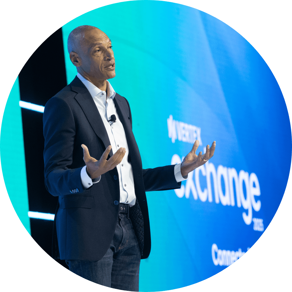 Chris Young, Chief Marketing Officer at Vertex Inc, gives a keynote from a vibrant blue stage.